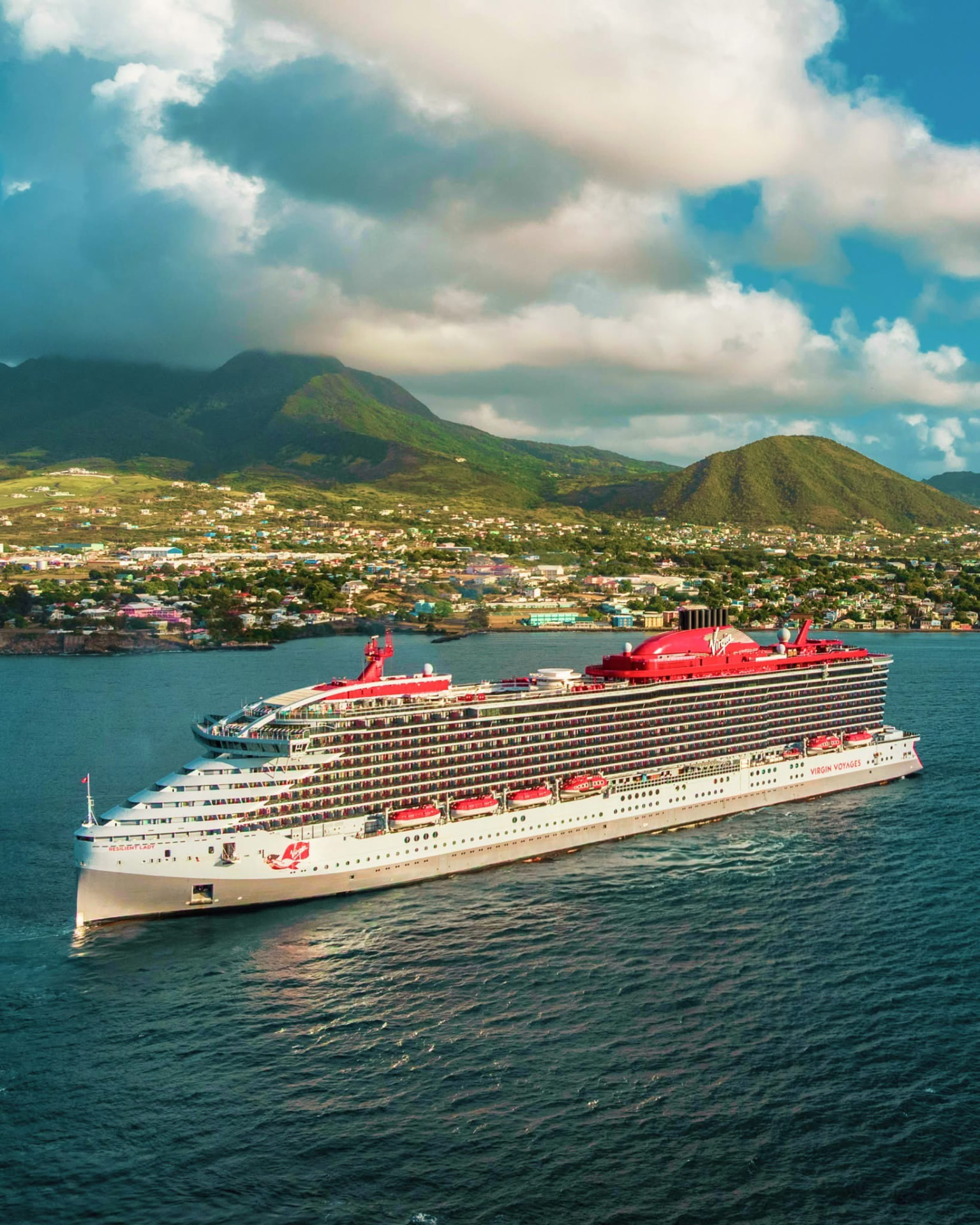 Virgin Voyages ship offshore beneath a shifting cloud deck